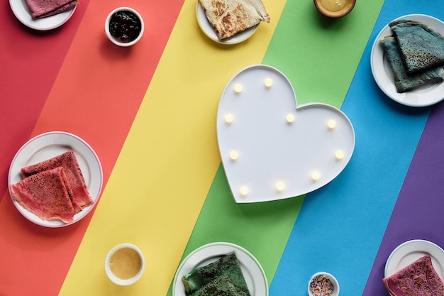 レインボー​パンケーキ​、​色違い​の​クレープ​。​ほうれん草​、​ビートルートパウダー​、​青い​抹茶​、​ターメリッククレープ​。​カラフル​な​パンケーキ​、​平らな​虹​の​層状​の​紙​の​上に​横たわっていた​。
