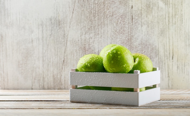 Rainy green apples in a wooden box on grunge and light wooden background.