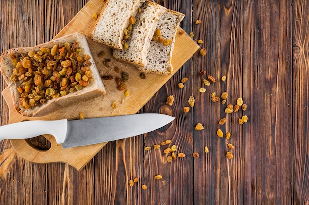 Foto gratuita uvetta sulle fette di pane con coltello affilato sul tagliere sopra il tavolo di legno