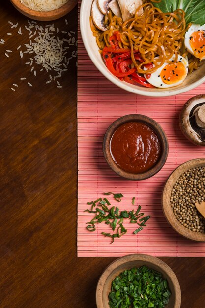 Ramen noodles with egg; salad; chives; coriander seeds; rice grain and sauce on wooden table