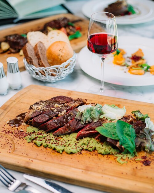 Rare cooked steak slices served with mashed avocado walnut lettuce spinach red wine