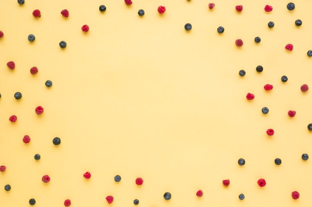 Raspberries and blueberries spread on yellow backdrop with copy space for writing the text