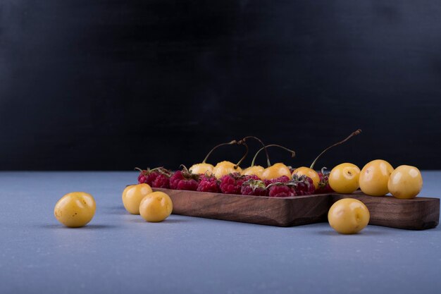 Raspberries and cherries in a wooden platter on dark background