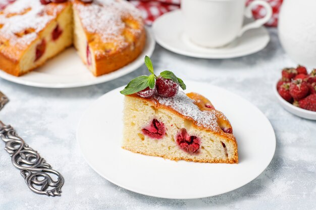 Raspberry cake with powdered sugar and fresh raspberries on a light . Summer berry dessert.