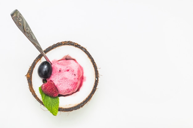 Raspberry ice cream inside the halved coconut with spoon against white background