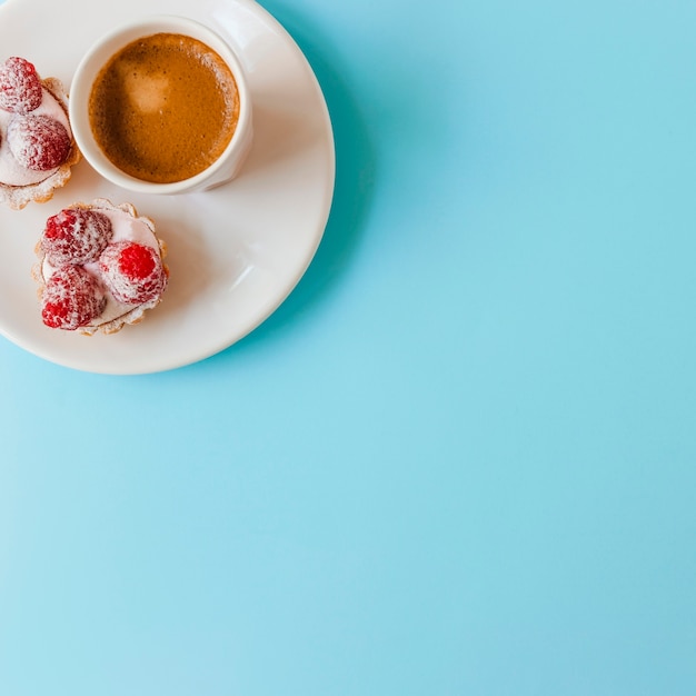 Raspberry tart with cream and coffee cup on plate over the blue background