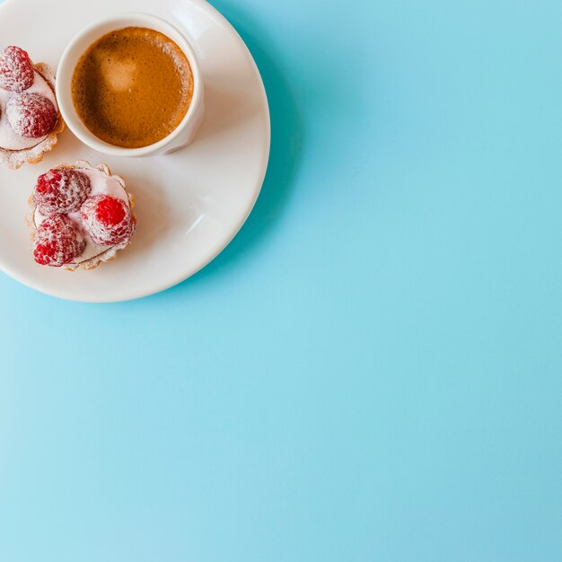 Raspberry tart with cream and coffee cup on plate over the blue background