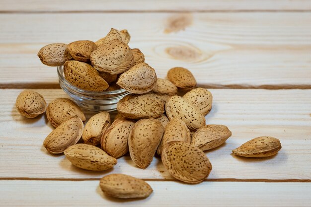 Raw almonds in the skin lies in a glass bowl and scattered on a wooden background, close-up