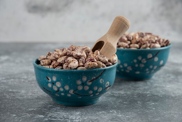 Raw bean grains displayed in bowls on marble surface.