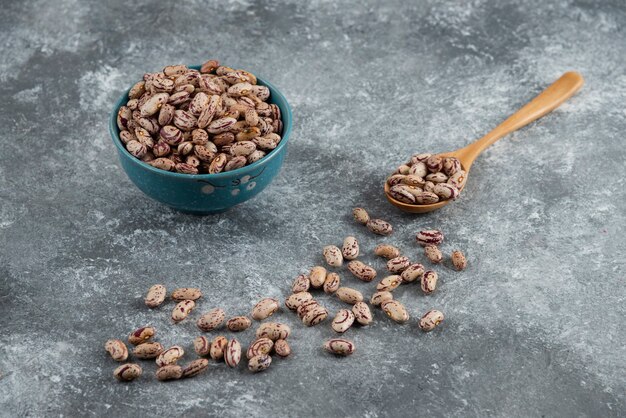 Raw beans and wooden spoon on marble.