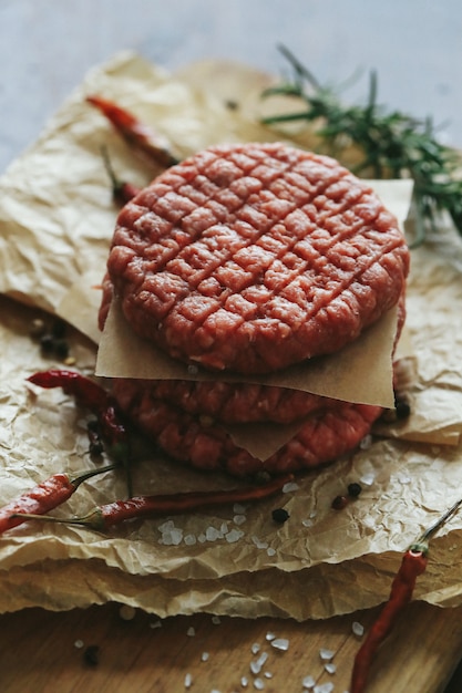Сырые говяжьи гамбургеры с травами и специями на темной грифельной тарелке