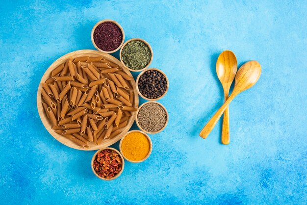 Raw brown past on wooden board and various kinds of spices over blue table.