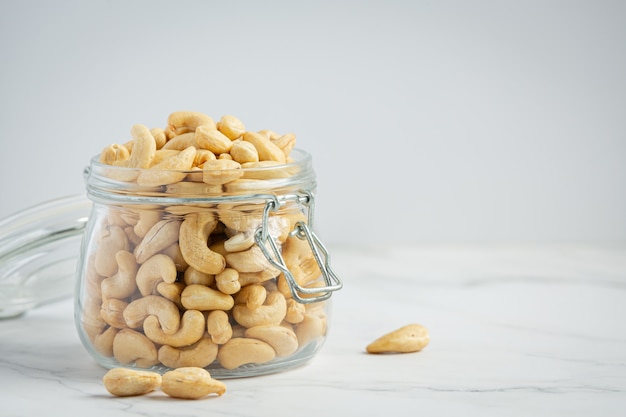 Raw cashews nuts in an open glass jar on marble background