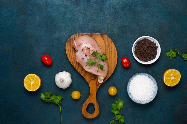 Raw chicken breast fillets on wooden cutting board with herbs and spices.top view