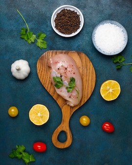 Raw chicken breast fillets on wooden cutting board with herbs and spices.top view