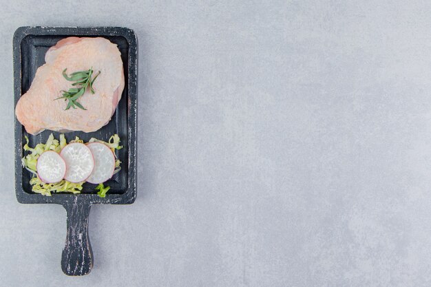 Raw chicken breasts and spices on the board, on the white surface