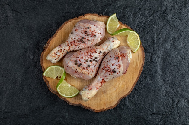 Raw chicken drumsticks on wooden board.