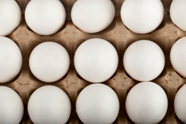 Raw chicken eggs in egg box on a marble surface.