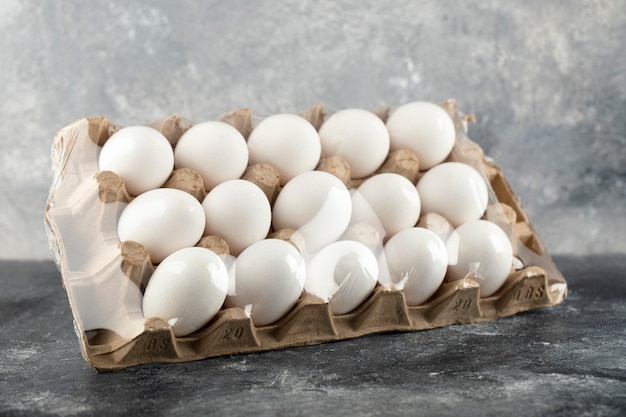 Raw chicken eggs in egg box on a marble surface. 