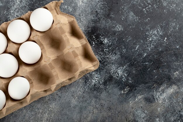 Raw chicken eggs in egg box on a marble surface.