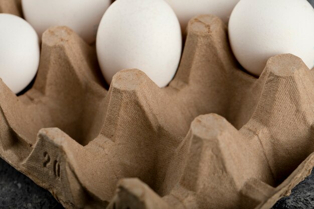 Raw chicken eggs in egg box on a marble surface. 