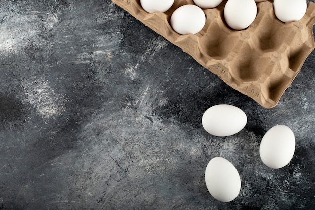 Raw chicken eggs in egg box on a marble surface.