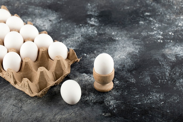 Сырые куриные яйца в яичной коробке на мраморной поверхности.
