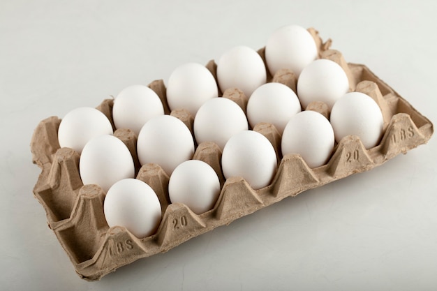 Raw chicken eggs in egg box on a white surface. 