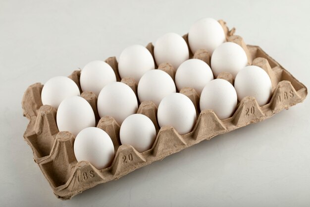 Сырые куриные яйца в яичной коробке на белой поверхности.