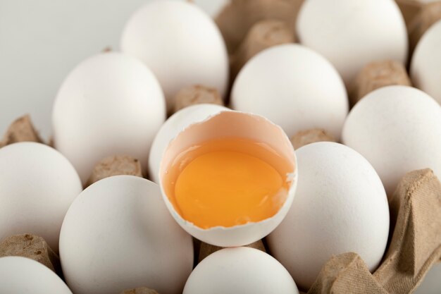 Raw chicken eggs in egg box on a white surface. 