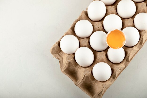 Raw chicken eggs in egg box on a white surface. 