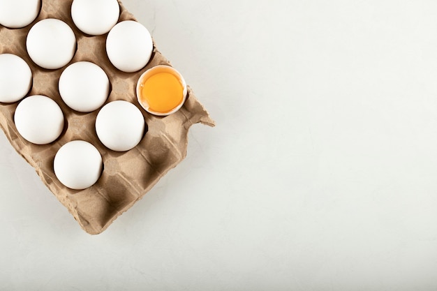 Raw chicken eggs in egg box on a white surface. 