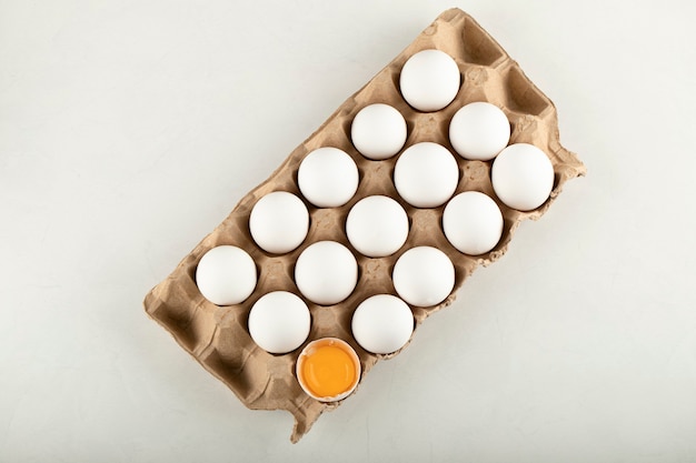 Raw chicken eggs in egg box on a white surface. 