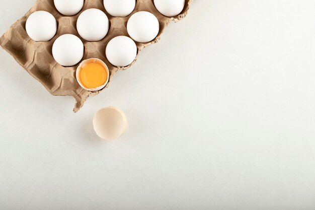 Raw chicken eggs in egg box on a white surface. 