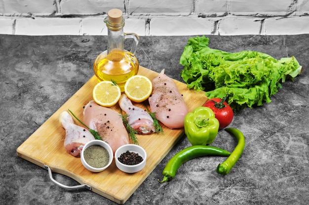 Free photo raw chicken fillet and legs on wooden plate with fresh vegetables, spices and glass of oil.