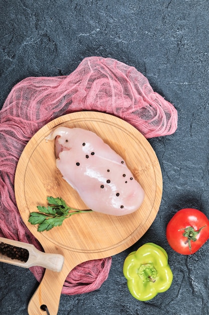 Free photo raw chicken fillet on wooden board with vegetables and tablecloth.