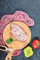 Free photo raw chicken fillet on wooden board with vegetables and tablecloth.