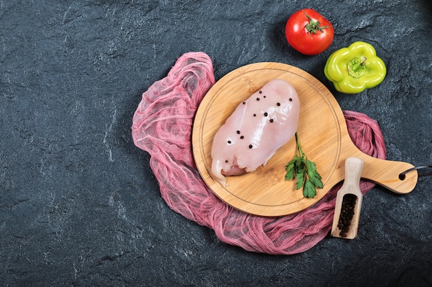 Raw chicken fillet on wooden board with vegetables and tablecloth.