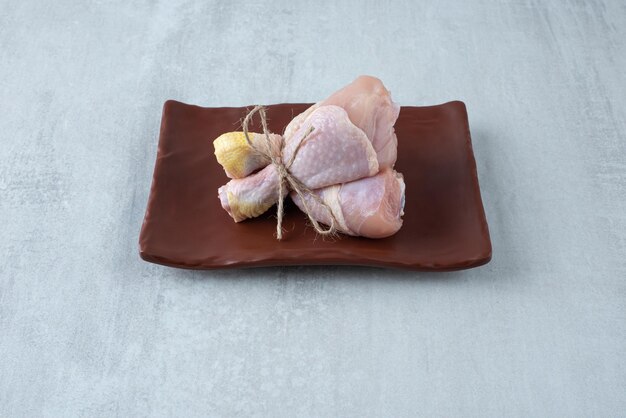 Raw chicken legs tied with rope on plate.