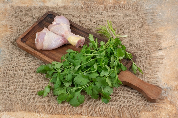 Raw chicken legs with greens on wooden cutting board on sackcloth