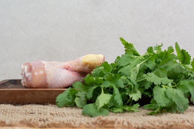 Raw chicken legs with greens on wooden cutting board .