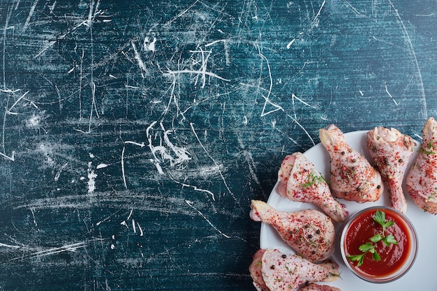 Raw chicken legs with herbs and spices and a cup of ketchup.