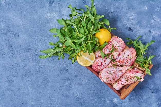 Raw chicken legs with spices on a wooden board on blue