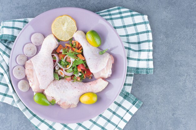 보라색 접시에 야채와 함께 원시 닭 다리입니다.