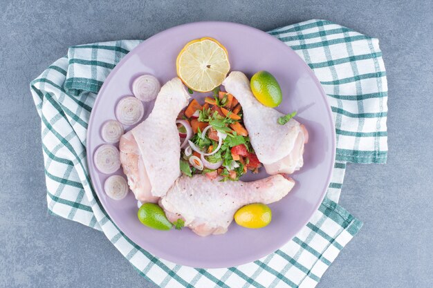 Raw chicken legs with vegetables on purple plate.