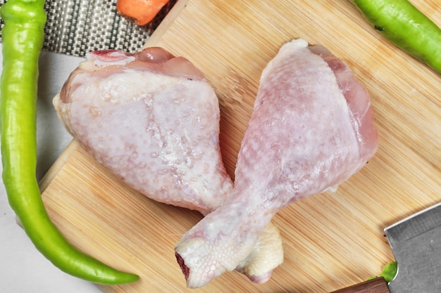 Raw chicken legs on wooden board with chili peppers