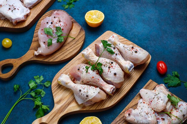 Raw chicken meat fillet, thigh, wings and legs with herbs ,spices,lemon and garlic on dark blue background. Top view