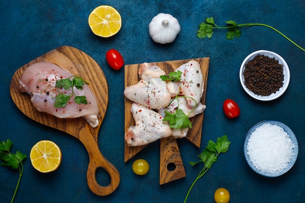 Raw chicken meat fillet, thigh, wings and legs with herbs ,spices,lemon and garlic on dark blue background. Top view