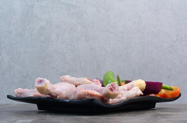 Сырое куриное мясо с перцем и луком на темной тарелке. Фото высокого качества