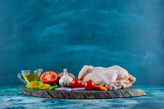 青い表面のボード上の生の鶏肉、野菜、油